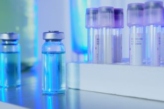 Frascos e tubos de ensaio com líquido azul em um laboratório sob luz fluorescente