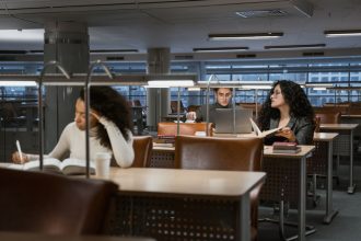 Estudantes universitários estudam com livros e laptops em uma biblioteca moderna.