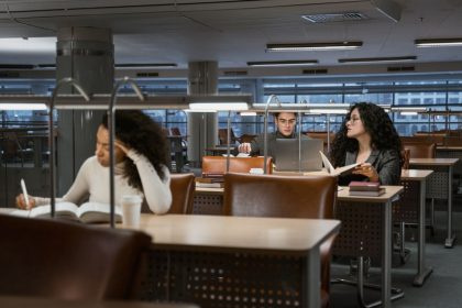 Estudantes universitários estudam com livros e laptops em uma biblioteca moderna.