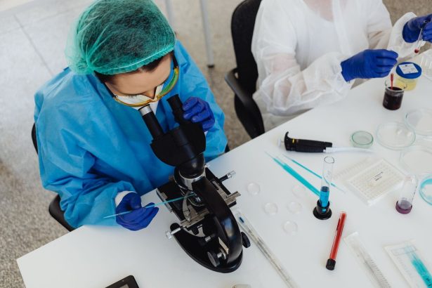 Pesquisadores usando equipamentos de proteção analisam amostras em um microscópio dentro de um laboratório.