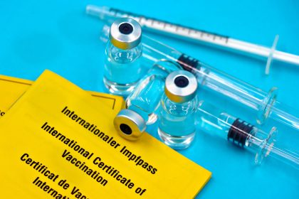 Frascos de vacina, seringas e certificados internacionais de vacinação dispostos sobre uma superfície azul.