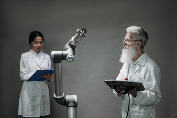 Dois pesquisadores de jaleco analisam um braço robótico em um laboratório.